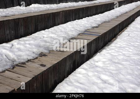 Fusione sulla neve primaverile sulle diverse superfici di vecchie tavole di legno marrone superficie esterna vista laterale primo piano Foto Stock