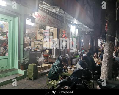 Hanoi, Vietnam. 26th Feb, 2023. Persone sedute sul marciapiede di fronte a un ristorante sulla strada. Credit: Alexandra Schuler/dpa/Alamy Live News Foto Stock