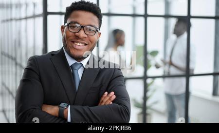 Attraente ragazzo con un sorriso affascinante e occhiali con le braccia ripiegate di fronte Foto Stock