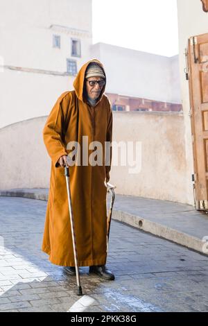 Un uomo anziano che indossa una djellaba tradizionale cammina lungo una strada a Fez Medina Marocco Foto Stock