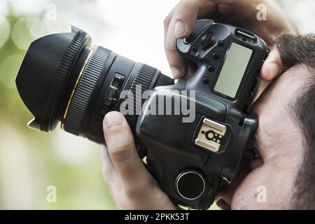 Un fotografo che guarda attraverso il mirino della sua fotocamera per catturare un'immagine Foto Stock