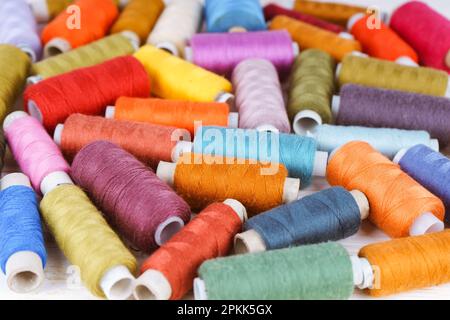 Dispersione di fili di cucitura di vari colori su fondo di legno bianco. Piano di giacitura, vista dall'alto. Foto Stock