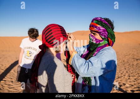 Una guida aiuta un turista americano a regolare il suo velo nel deserto del Sahara Foto Stock