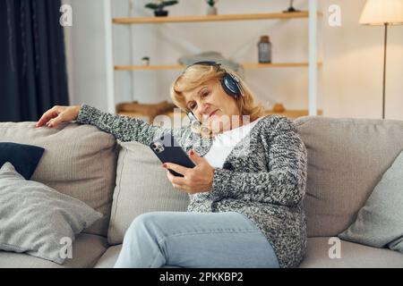 Ascolto di musica con le cuffie. Donna anziana con capelli biondi è a casa. Foto Stock