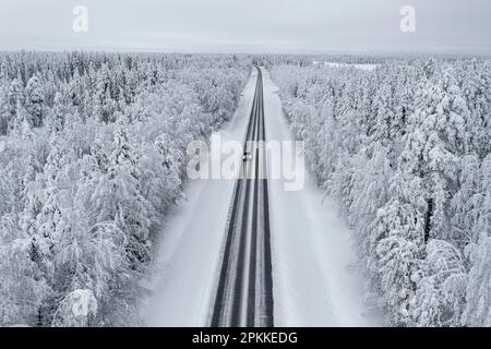 Vista dall'alto della vettura che guida su una strada vuota scivolosa nella foresta innevata, in Lapponia, Finlandia, Europa Foto Stock