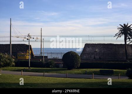 Ferrovia sul mare al tramonto visto da un parco e incorniciato da alberi e ringhiere Foto Stock