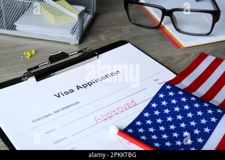 Modulo di richiesta visto con parola approvata e bandiera americana su tavolo di legno, primo piano Foto Stock