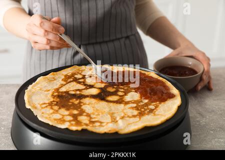 Donna che cucina deliziosa crepe con marmellata su elettrico frittella in cucina, primo piano Foto Stock