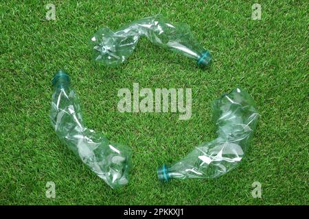 Simbolo di riciclaggio in bottiglie di plastica stropicciate su erba verde, a giacitura piatta Foto Stock