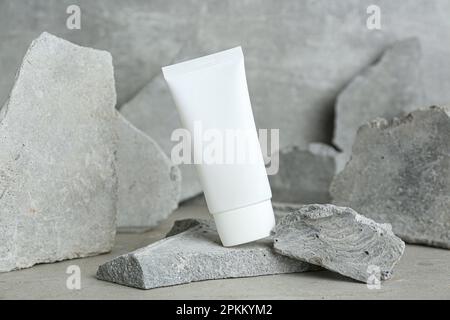 Tubo di crema per le mani tra le pietre su sfondo grigio. Modello per il design Foto Stock