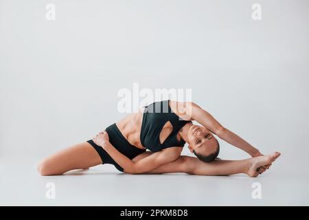 Tendendo al lato. Giovane donna in abiti sportivi che fanno ginnastica in interni. Foto Stock
