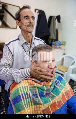 Un turista americano che ottiene un rasoio diritto e un taglio di capelli in un barbiere a Marrakech Marocco Foto Stock
