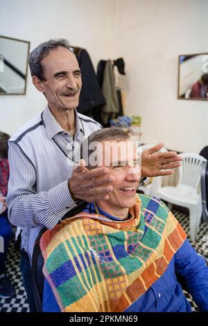 Un turista americano che ottiene un rasoio diritto e un taglio di capelli in un barbiere a Marrakech Marocco Foto Stock