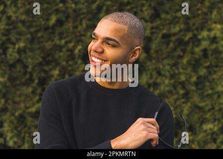 Primo piano medio di un giovane afro-americano che tiene occhiali da sole e che guarda oltre, all'aperto. Foto di alta qualità Foto Stock