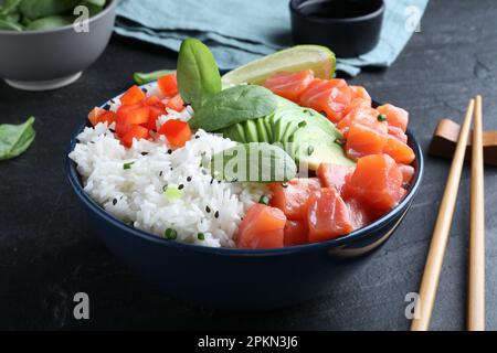 Deliziosa ciotola di poke con salmone, spinaci e avocado servita sul tavolo nero Foto Stock