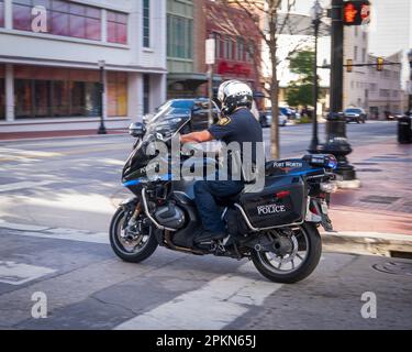 Un poliziotto su una motocicletta nera, indossando un casco e un'uniforme completa, è visto in viaggio lungo una strada trafficata della città in servizio. Foto Stock