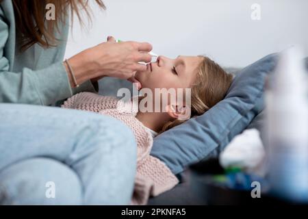 Madre spray nasale farmaci per la figlia malata. Foto Stock