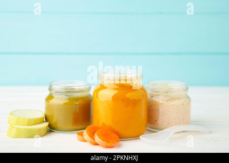 Vasetti di vetro con alimenti nutrienti per bambini su sfondo blu. Purea di verdure con cucchiaio. Foto Stock