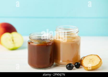 Vasetti di vetro con alimenti nutrienti per bambini su sfondo blu. Purea di frutta e verdura Foto Stock