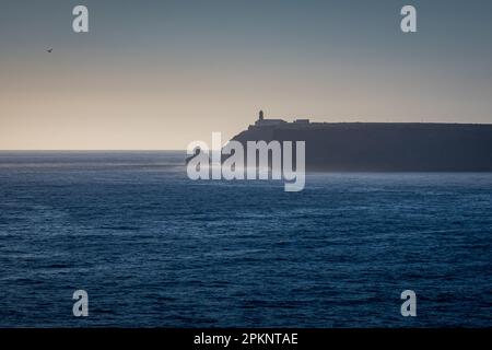 Vista al crepuscolo da Sagres a Capo Cabo de São Vicente con l'iconico faro di Farol do Cabo de São Vicente e un lontano gabbiano solitario che vola. Foto Stock