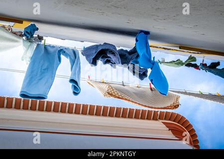 Lavaggio fresco e pulito che sbatte nella brezza su due clotheslines steso lungo uno stretto vicolo in Portogallo, con un cielo blu e nuvole bianche. Foto Stock