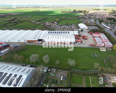 Vista drone di un magazzino di logistica e distribuzione. Mostra rimorchi HGV parcheggiati in un parco camion con un campo sportivo annidato tra gli edifici. Foto Stock