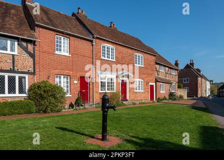 Il villaggio di Southwick in Hampshire, Inghilterra, ben noto per avere porte rosse su ogni casa tranne le case padronali. Pompa dell'acqua in primo piano. Foto Stock