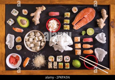 Set di piatti tradizionali giapponesi su sfondo scuro. Sushi, nigiri, bistecca di salmone crudo, riso, formaggio spalmabile, avocado, lime, zenzero sottaceto (gari) Foto Stock
