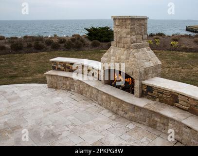 Camino in pietra che brucia su un patio di pietra di pavimentazione presso la baia in un cortile residenziale. Foto Stock