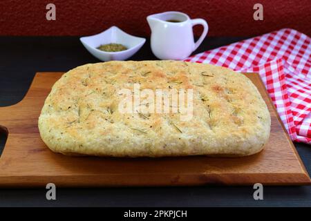 Delizioso pane di focaccia alle erbe di produzione italiana appena sfornato su tavola da pane di legno Foto Stock