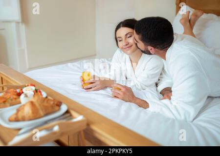 Marito Kissing moglie bere succo sdraiato in camera d'albergo Foto Stock