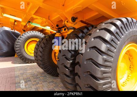 Enormi ruote posteriori del dumper a cassone ribaltabile con angolazione insolita in primo piano. Le ruote sono dotate di un battistrada per il movimento del dumper su terreni sfusi. Foto Stock