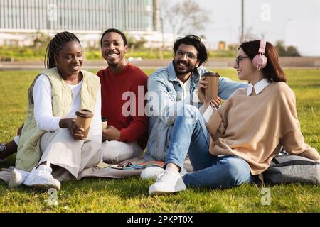 Allegri studenti moderni multietnici millenari con una tazza di caffè da asporto studiano insieme, riposano dalla lezione Foto Stock