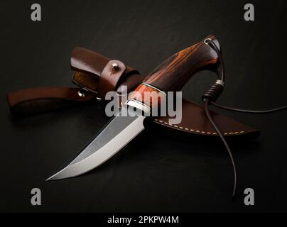 Coltello da caccia fatto a mano su sfondo nero. Fodero in pelle fatto a mano Foto Stock
