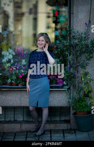 Una donna si trova sulla strada vicino alla finestra di un negozio di fiori. Foto Stock