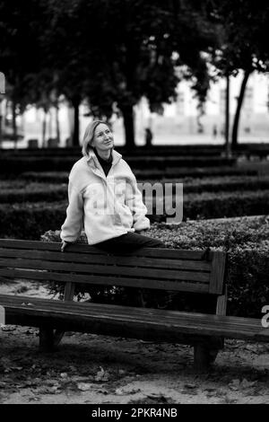 Una donna siede sul retro di una panchina del parco. Foto in bianco e nero. Foto Stock