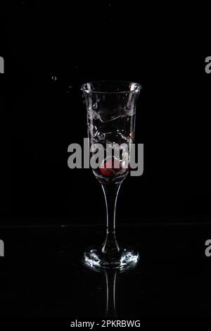 Un bicchiere d'acqua e una ciliegia che cadono nell'acqua. Foto di alta qualità Foto Stock