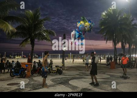 Il venditore di palloncini giocattolo smette di lavorare per alcuni minuti per giocare con una palla da calcio con un collega sul lungomare di Copacabana. Stile di vita di Rio de Janeiro, Brasile. Foto Stock