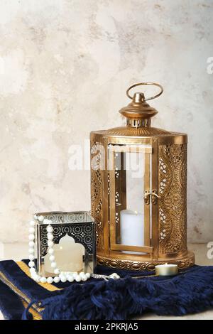 Lampade musulmane con candele accese e perline di preghiera sul tappeto vicino al muro di grunge Foto Stock