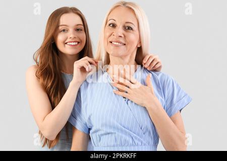 Giovane donna che mette la collana intorno al collo della madre su sfondo grigio Foto Stock