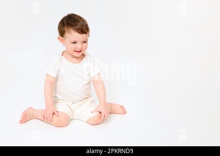 Un bambino felice è seduto su uno studio sfondo bianco. Ritratto completo di un bambino sorridente. Bambino di circa due anni (un anno nove mesi) Foto Stock