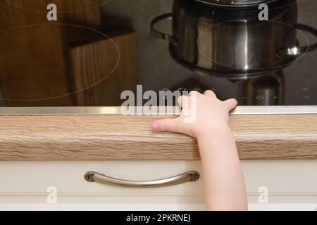 Il bambino salite su una stufa elettrica calda nella cucina domestica. Un bambino piccolo tocca la superficie della stufa con la mano al rischio di ottenere b Foto Stock