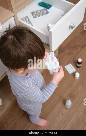 Il bambino del bambino ha aperto il cassetto dell'armadietto con le pillole e la medicina. Bambino che tiene una confezione di pillole nel salotto di casa. Bambino di età un anno nove mese Foto Stock