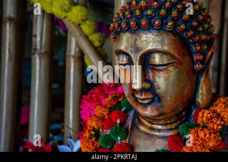 Primo piano della statua di buddha di bronzo seduta in meditazione con decorazioni floreali per la cerimonia del festival. Foto di alta qualità Foto Stock