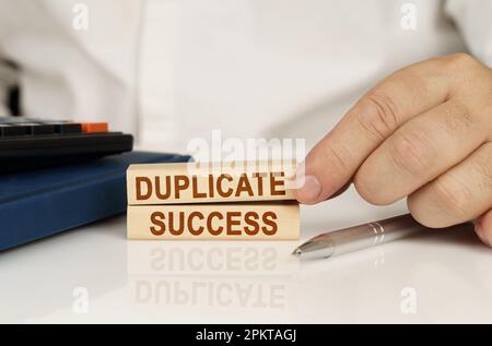 Concetto aziendale. Nelle mani di un uomo d'affari, blocchi di legno con l'iscrizione - Duplicate Success, accanto a un notebook e una calcolatrice. Foto Stock