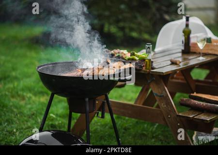 Il braciere fumante di una forma rotonda. La legna da ardere si accende nel braciere sullo sfondo di un tavolo e sedie. Il concetto di pic-nic, relax Foto Stock