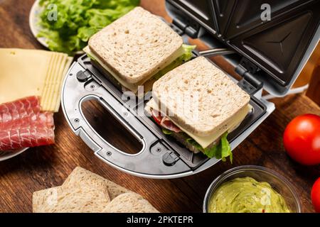 Paninoteca e vari ingredienti su sfondo di legno. Cottura di panini con farciture diverse. Foto Stock