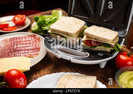 Cottura di panini con farciture diverse. Paninoteca e vari ingredienti su sfondo di legno. Foto Stock