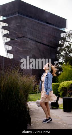 Asian Teen con capelli che soffiano nel vento in piedi davanti alla Torre del Museo De Young | Donna | Abito corto | giacca in denim Foto Stock