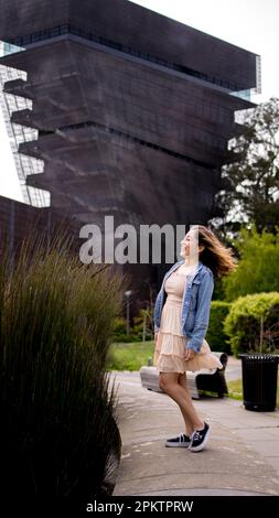 Asian Teen con capelli che soffiano nel vento in piedi davanti alla Torre del Museo De Young | Donna | Abito corto | giacca in denim Foto Stock